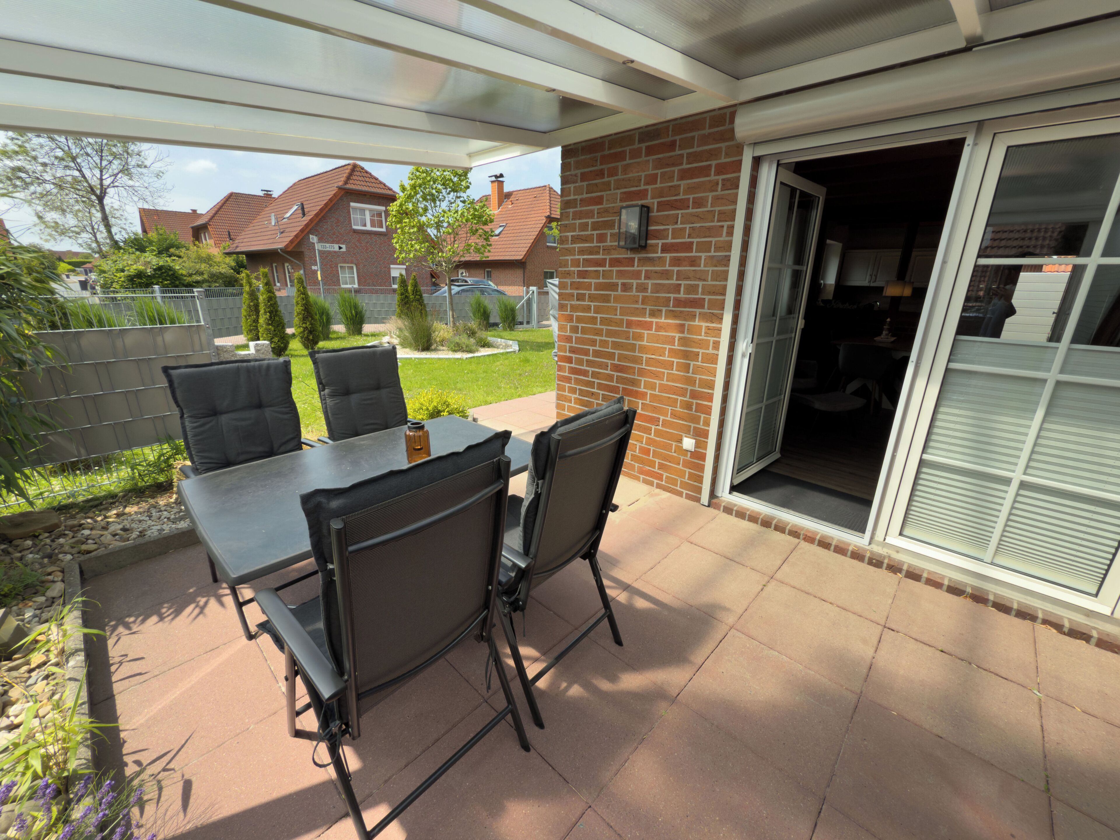 Une terrasse extérieure avec une table et des chaises, un mur en briques et une porte-fenêtre coulissante donnant sur un espace abrité.