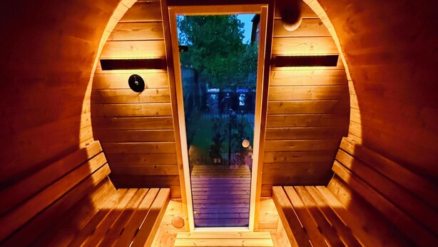 Una sauna de madera con techo abovedado, un banco y una puerta que da al exterior.
