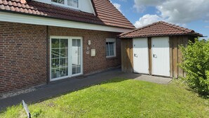 A two-story brick house with a red-tiled roof, a front porch, and a small garden. - Pelikan vacation apartment (Hooksiel)