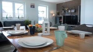 Un coin repas avec une table en bois dressée pour quatre personnes, une lanterne blanche et un vase rempli de fleurs.