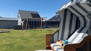 Un jardin avec une balançoire en bois, un espace de détente couvert et une cour clôturée.