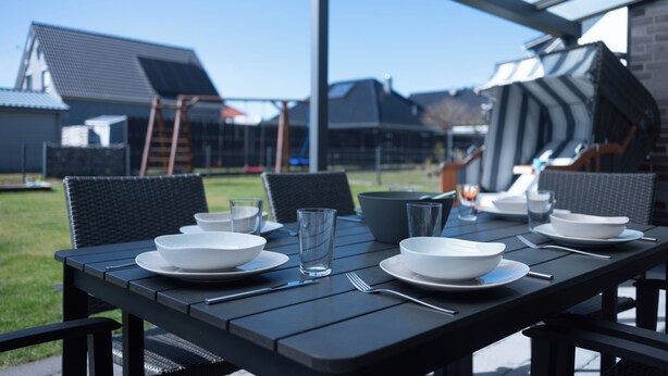 Un espace extérieur abrité, aménagé pour les repas, avec une table dressée pour quatre personnes, entourée de chaises.