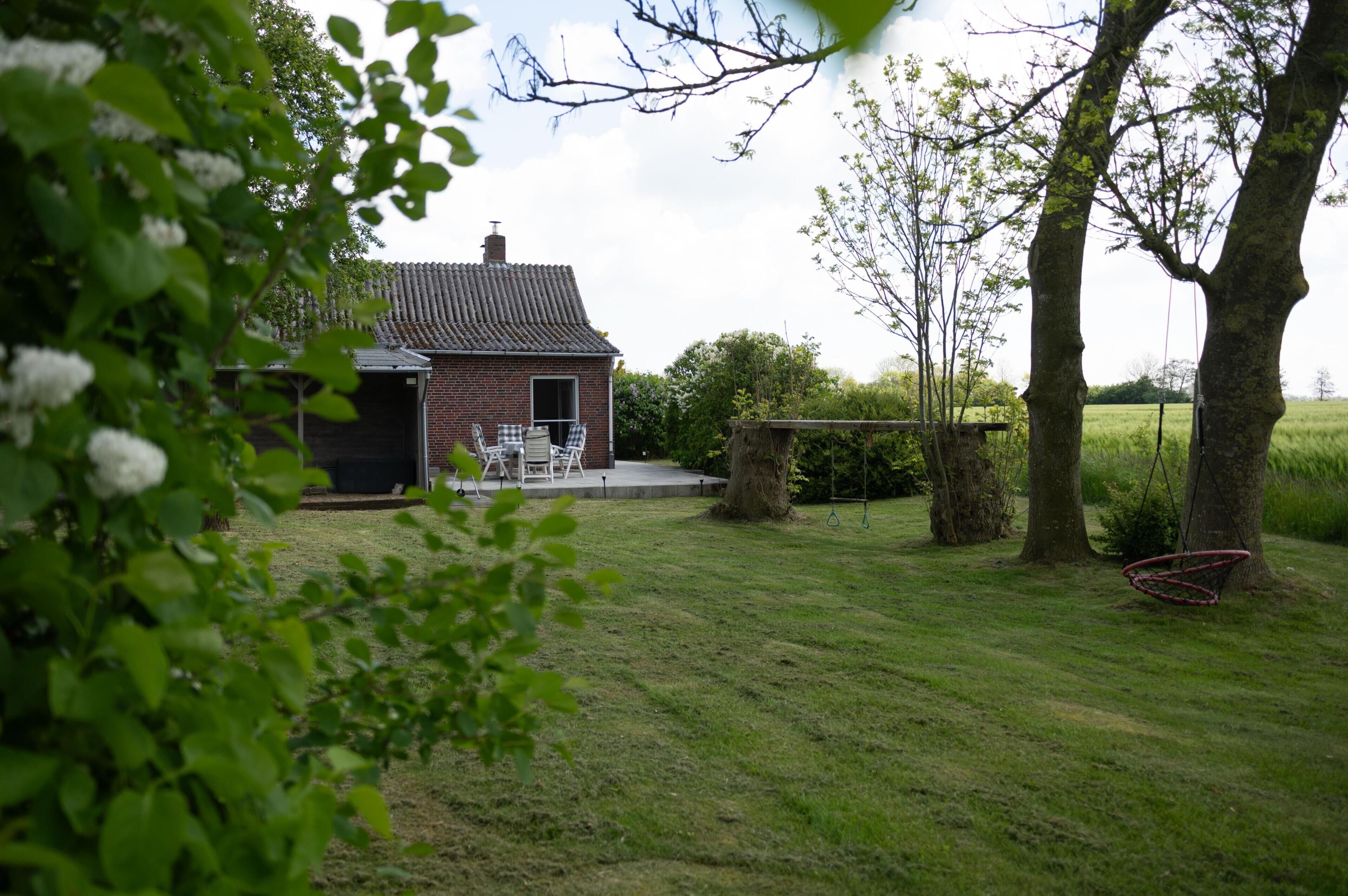 A brick house with a tiled roof, a patio with outdoor furniture, and a swing set.