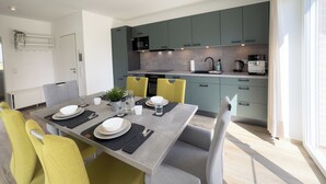 A modern kitchen with grey cabinets, a dining table set with plates, glasses, and cutlery, and yellow chairs. - The "Genießerei" vacation apartment on the Wangermeer invites you to relax with its terrace, dog-friendly atmosphere and wallbox at the parking space. (Wangerland)