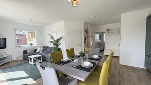 A modern living space with a dining area, a sofa, a TV, and a plant. - The "Genießerei" vacation apartment on the Wangermeer invites you to relax with its terrace, dog-friendly atmosphere and wallbox at the parking space. (Wangerland)
