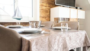 A dining area with a table set for two, a television above the cabinets, and a wooden wall. - Modern vacation apartment in Hooksiel with sunny balcony, two bedrooms, attic reading corner and quiet, central location near the North Sea. (Hooksiel)