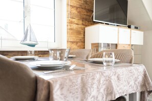 A dining area with a table set for two, a television above the cabinets, and a wooden wall. - Modern vacation apartment in Hooksiel with sunny balcony, two bedrooms, attic reading corner and quiet, central location near the North Sea. (Hooksiel)