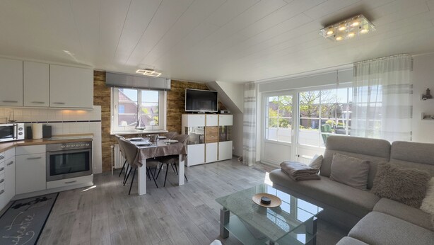 A modern kitchen with white cabinets, a dining table, and a large window. - Modern vacation apartment in Hooksiel with sunny balcony, two bedrooms, attic reading corner and quiet, central location near the North Sea. (Hooksiel)