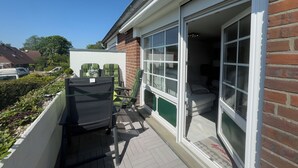 A residential building with a patio area, a sliding glass door, and a white exterior wall. - Modern vacation apartment in Hooksiel with sunny balcony, two bedrooms, attic reading corner and quiet, central location near the North Sea. (Hooksiel)