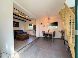 Ein modernes Wohnzimmer mit Sofa, Couchtisch, Essbereich mit Tisch und Stühlen, Fernseher und Treppe mit Geländer.
