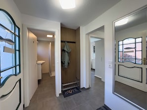 Ein Flur mit einer zur Toilette führenden Tür, einem Kleiderständer und einer Fußmatte mit dem Schriftzug 'HOME'.