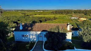 Un bâtiment blanc, doté d’un toit en tuiles, entouré de verdure et de champs.