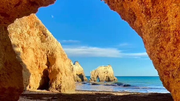 Une plage avec une formation rocheuse naturelle qui s’étend en arc au-dessus du sable.