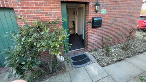 A brick building with a green door, a mailbox, and a welcome mat. - Cozy vacation home with garden, terrace and central location - the "Kleine Hookie" in Hooksiel offers relaxation for couples, families and dog owners. (Hooksiel)