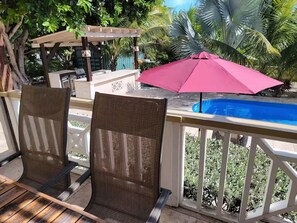 A deck with two wicker chairs, a pink umbrella, and a pool. - Tropical Carabas Villa in Grace Bay Beach (Grace Bay)