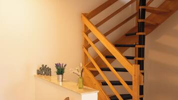 Un escalier en bois avec une rampe, une petite étagère ornée d’objets décoratifs et un luminaire fixé au mur.