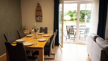 Un coin repas avec une table en bois dressée pour quatre personnes, des chaises et une vue sur une terrasse extérieure, accessible par une porte vitrée.