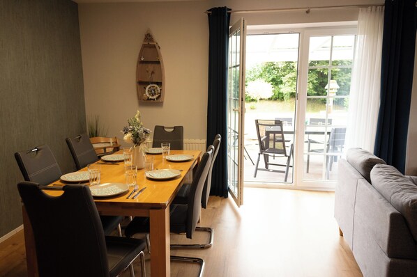 Un coin repas avec une table en bois dressée pour quatre personnes, des chaises et une vue sur une terrasse extérieure, accessible par une porte vitrée.