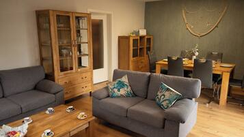 Un salon comprenant un canapé, un meuble en bois, une table à manger avec des chaises et un élément décoratif mural.