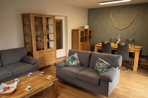 Un salon comprenant un canapé, un meuble en bois, une table à manger avec des chaises et un élément décoratif mural.