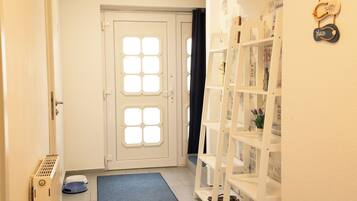 Un couloir avec une porte blanche, un radiateur, une moquette bleue et une étagère blanche contenant des magazines.