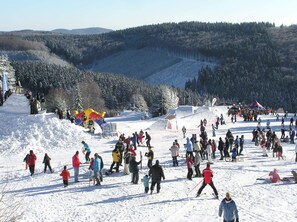 Area innevata all'aperto con persone che sciano e passeggiano.