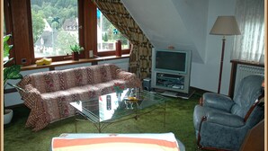 Un salon comprenant un canapé, une table basse en verre, un téléviseur, un fauteuil et une fenêtre avec des rideaux.