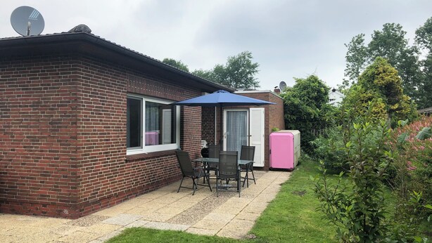 A brick house with a patio, a table with chairs, a pink refrigerator, and a satellite dish. - Bungalow close to the beach in Schillig with garden, three bedrooms, two bathrooms, up to three parking spaces and dog-friendly facilities - ideal for families and friends. (Schillig)