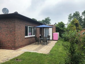 Uma casa de tijolos com um pátio, uma mesa com cadeiras, uma geladeira rosa e uma antena parabólica.