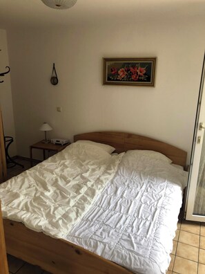 Ein Bett mit Holz Kopfteil, einer weißen Bettdecke und einem kleinen Nachttisch mit Lampe.