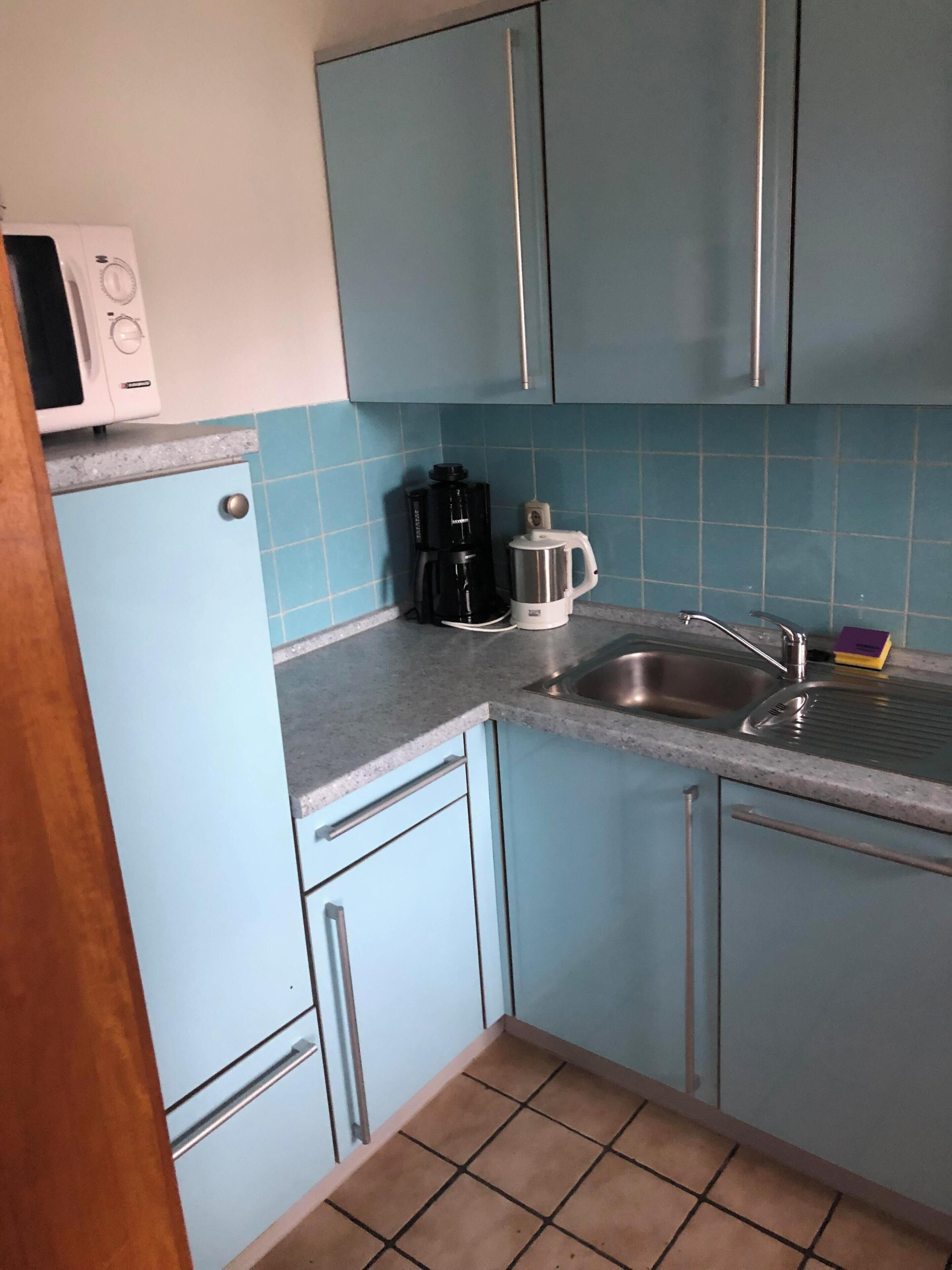 A kitchen with blue cabinets, a white microwave, a coffee maker, and a sink.