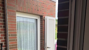 A room with a sliding glass door, a brick wall, a white door with louvered glass, and a concrete step leading to the door. - Bungalow close to the beach in Schillig with garden, three bedrooms, two bathrooms, up to three parking spaces and dog-friendly facilities - ideal for families and friends. (Schillig)