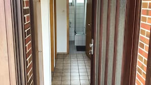 A hallway with a tiled floor, a door with a glass panel, and a view into a bathroom with a shower and tiled walls. - Bungalow close to the beach in Schillig with garden, three bedrooms, two bathrooms, up to three parking spaces and dog-friendly facilities - ideal for families and friends. (Schillig)