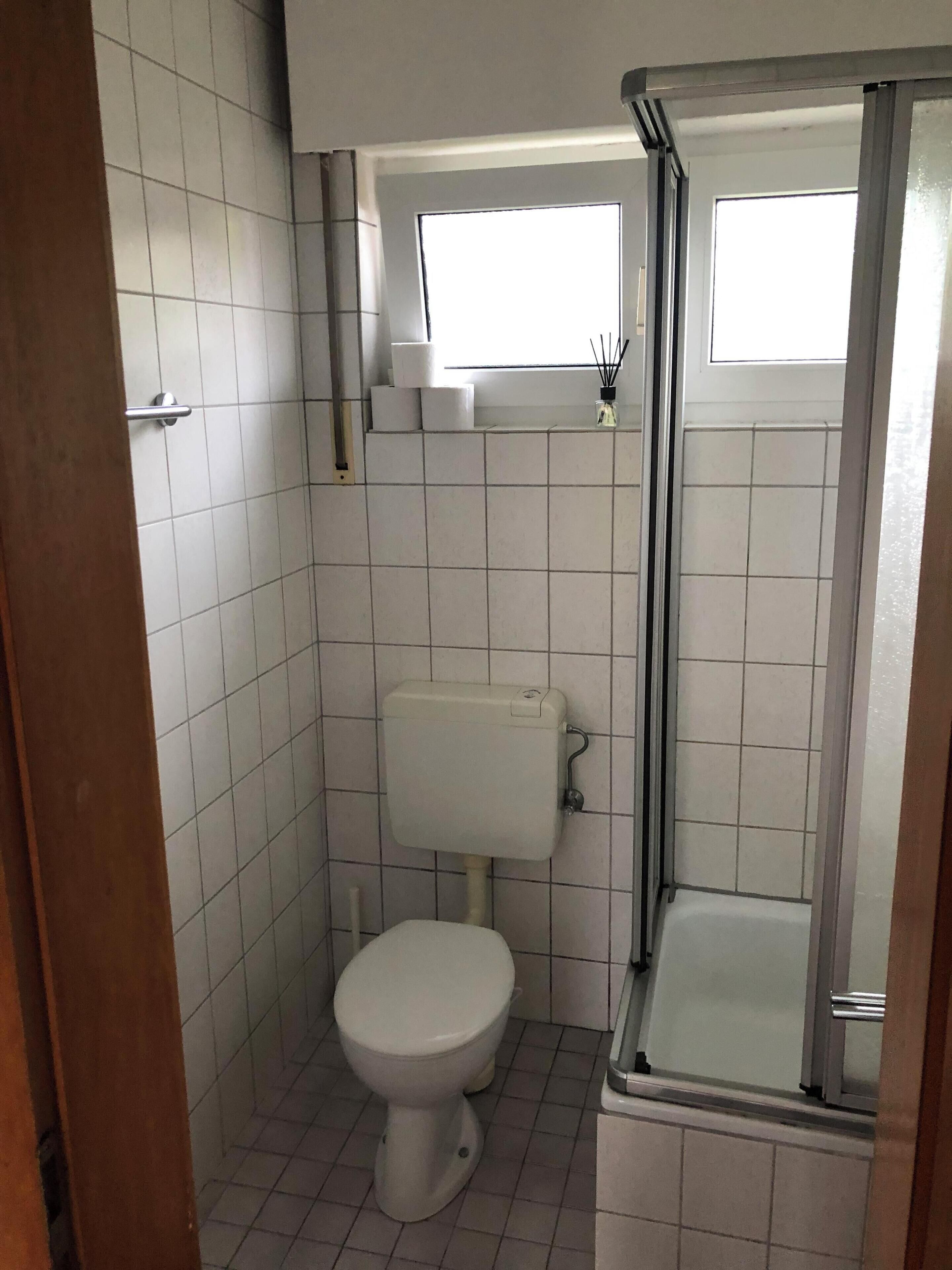 A small bathroom with a toilet, a window, and a shower area.