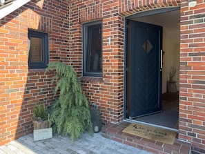 A brick building with a dark blue door, a window, and a doormat. - Detached vacation home with large, fenced garden, wood-burning stove, three bedrooms and quiet location near the North Sea - ideal for families and dog owners. (Wangerland)