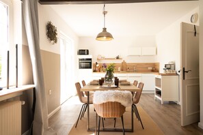 A modern kitchen with a dining area, wooden cabinets, a hanging light fixture, and a view of the outdoors. - Detached vacation home with large, fenced garden, wood-burning stove, three bedrooms and quiet location near the North Sea - ideal for families and dog owners. (Wangerland)