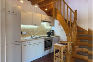 A kitchen with white cabinets, a wooden staircase, and a tiled backsplash. - Cozy semi-detached house in Hooksiel with fireplace, garden, three bedrooms, two bathrooms and dog-friendly furnishings - ideal for a family vacation by the North Sea. (Hooksiel)