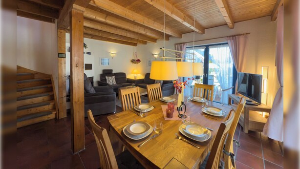 Een eethoek met een houten tafel voor vier personen, omringd door stoelen, met een trap naar een hoger niveau.
