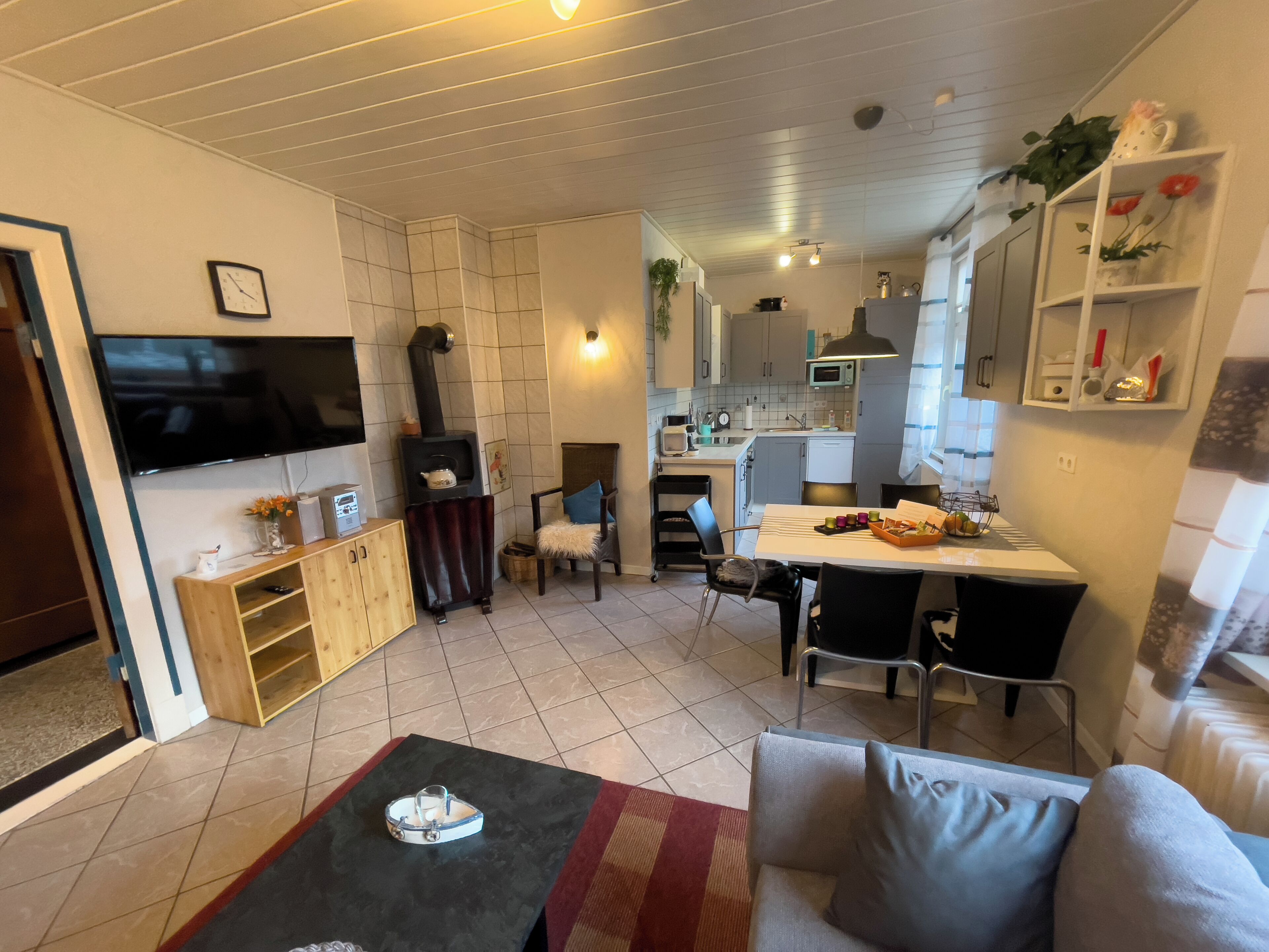 Ein modernes Wohnzimmer mit Flachbildfernseher, Kamin, Essbereich mit Tisch und Stühlen sowie Küche im Hintergrund.