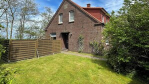 A brick house with a red roof, a wooden fence, and a well-maintained lawn.