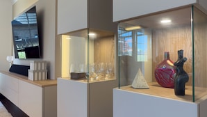 A modern living room with a flat-screen TV mounted on the wall, a glass display case with decorative items, and a wooden floor. - Modern vacation home directly on the Wangermeer. Comfort and maritime flair for families, couples and dog owners. (Wangerland)