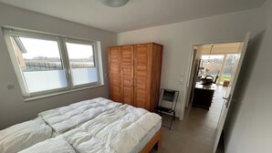 Een slaapkamer met een bed, een kledingkast, een stoel en uitzicht door een raam.