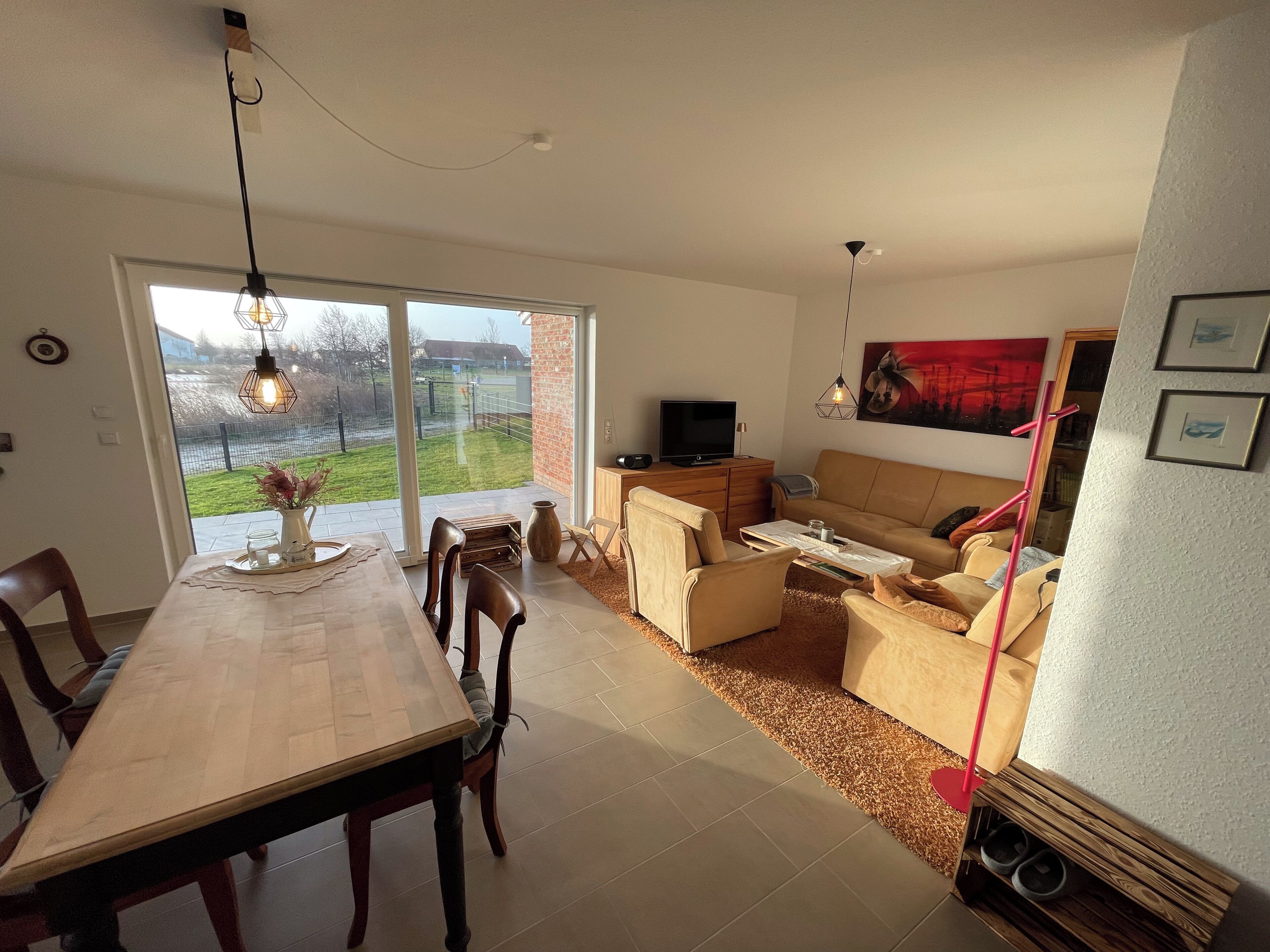 A modern living room with a dining area, a sofa set, a TV, and a large window with a view of the outdoors.
