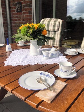 A wooden table set with white plates, cups, and a pitcher of flowers, with a brick wall and windows in the background. - Home port Wangermeer (Wangerland)