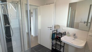 Een badkamer met een douchecabine van glas, een wit wastafeltje en een spiegel erboven.