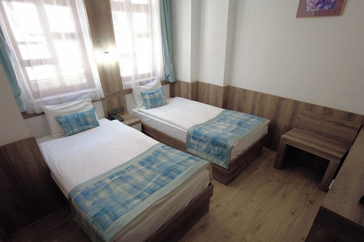 A room with two beds, a wooden floor, and a window with curtains.