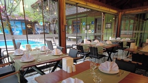 A restaurant with tables set for dining, a pool visible through the windows, and a view of the outside. - Oscar Boutique Hotel (Antalya)