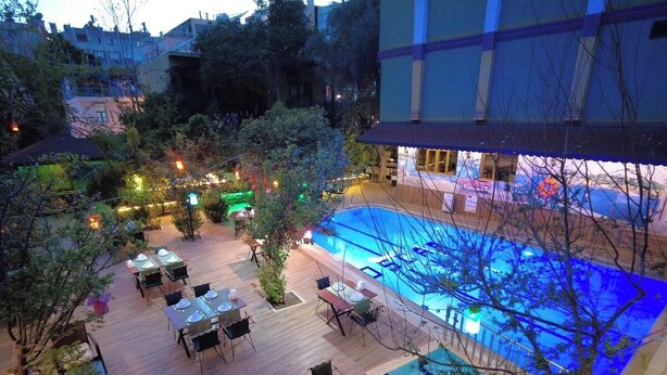 An outdoor pool area with tables and chairs, surrounded by trees and buildings. - Oscar Boutique Hotel (Antalya)