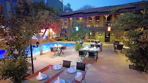 An outdoor dining area with tables set for guests, a pool, and a building with balconies in the background. - Oscar Boutique Hotel (Antalya)