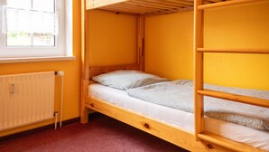 Camera con letto a castello, finestra, termosifone e pavimento rivestito di moquette rossa.